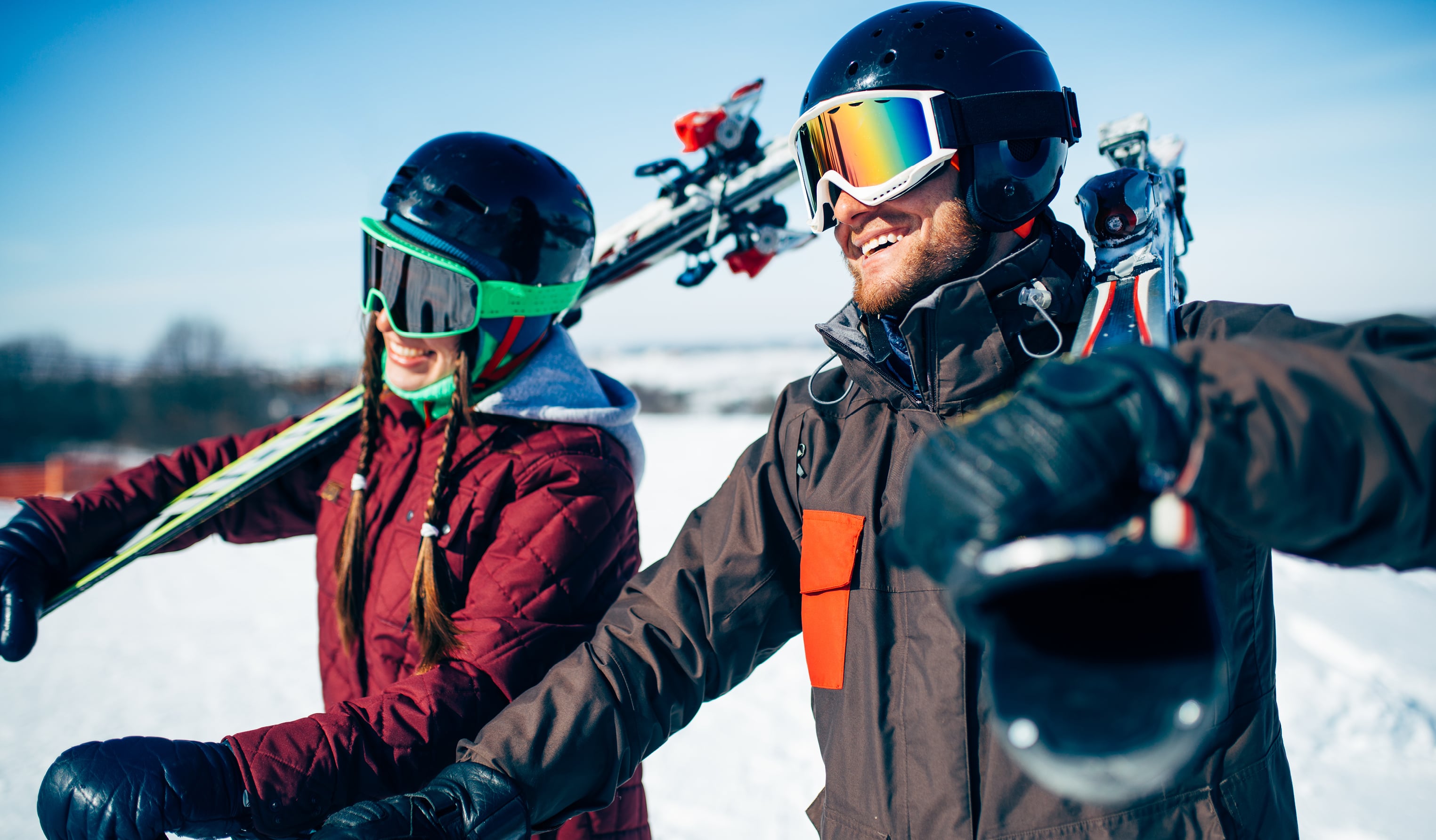 Two smiling skiers carrying skis on their shoulders in the snow